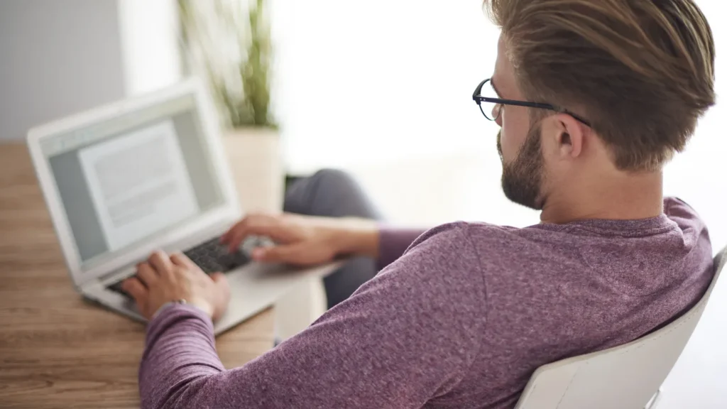 Uomo di spalle al lavoro su un portatile alla scrivania di casa